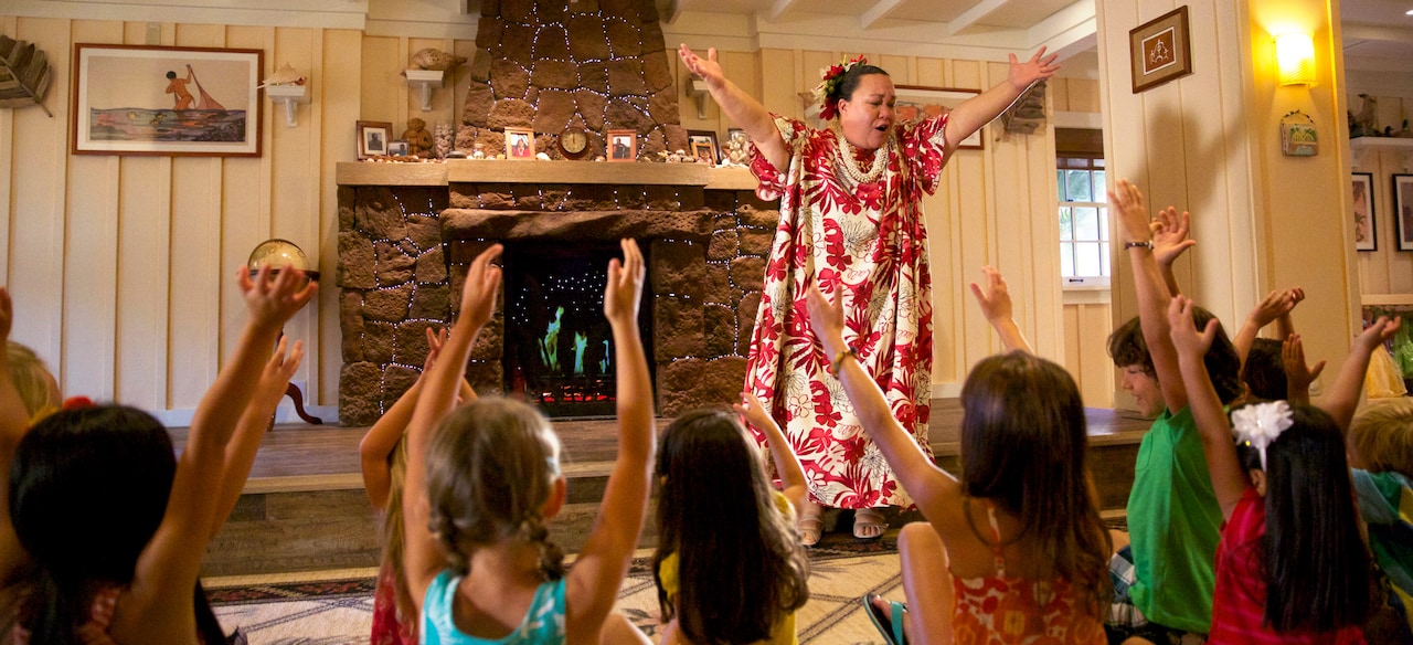 A woman in traditional Hawaiian dress leads a group of children in song and movement