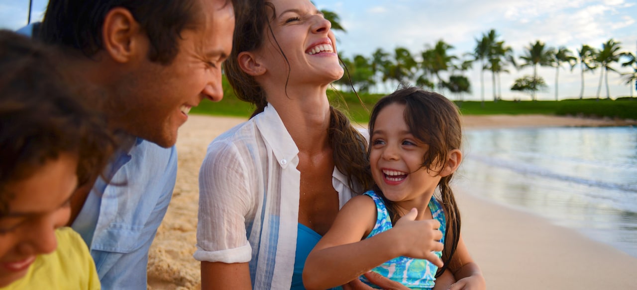 A family sitting on a sandy beach smile and laugh together