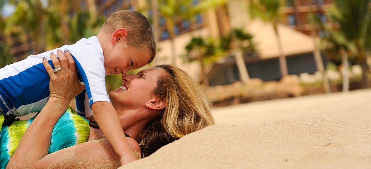 ビーチに仰向けになり、抱っこした小さな息子の鼻に自分の鼻をつけて微笑む母親