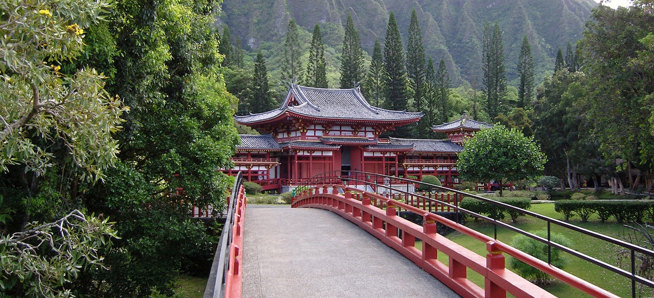 A wooden bridge leading to a temple situated in a verdant valley