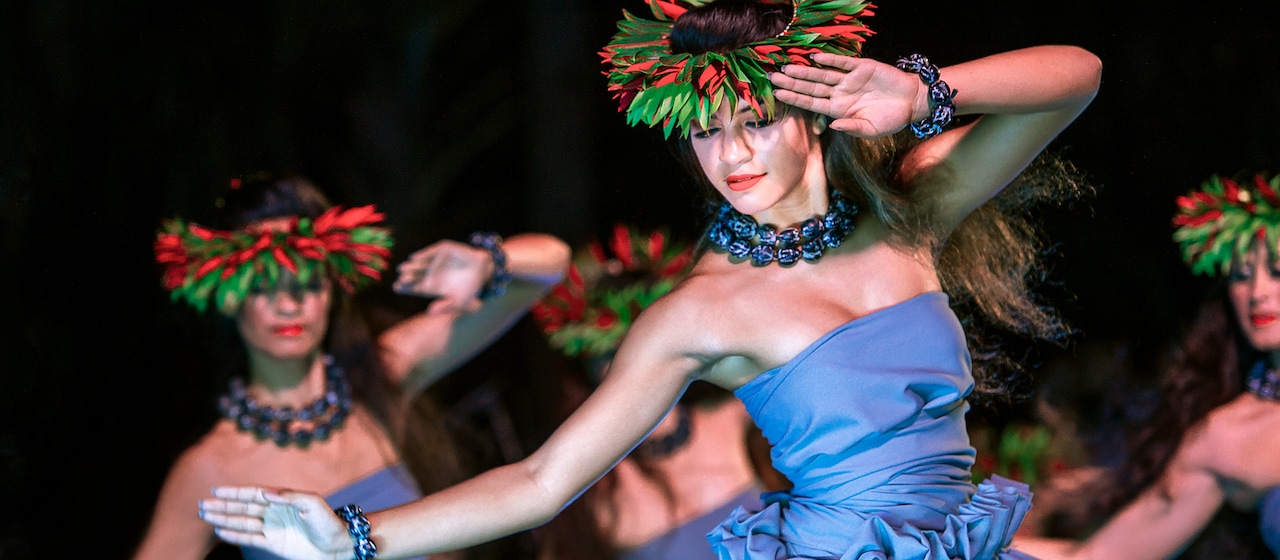 A group of Hawaiian women in traditional outfits and leafy head dresses perform an island dance at the Ka Wa'a Luau.