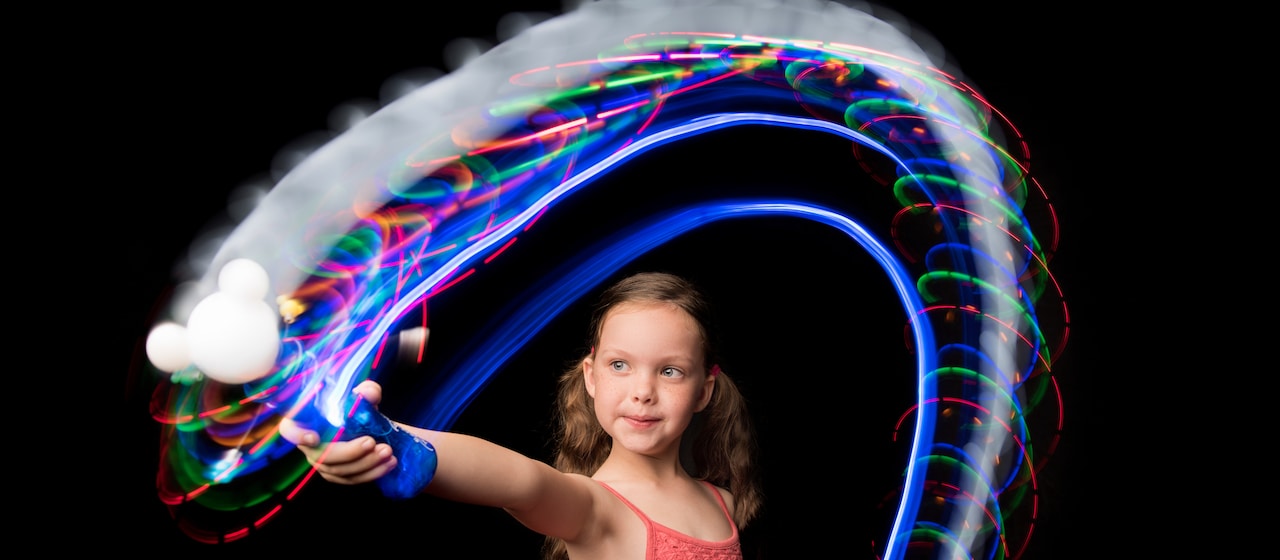 A young girl waves a Mickey Mouse light wand that creates a trail of lights behind it