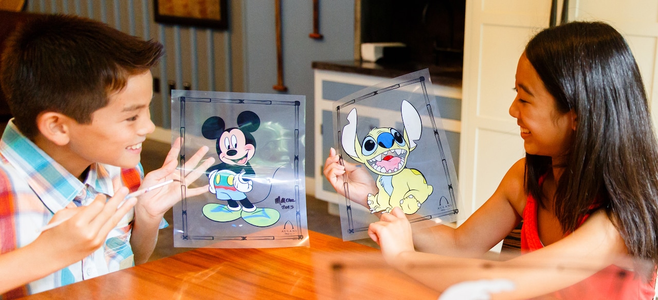 A boy and a girl show each other Disney character animation cels they have painted