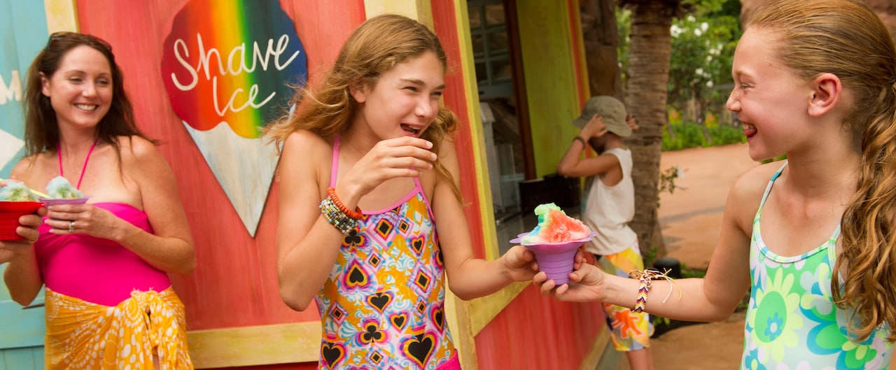 Two tween girls in swimwear clutching a shave ice dessert as a woman holding a shave ice looks on