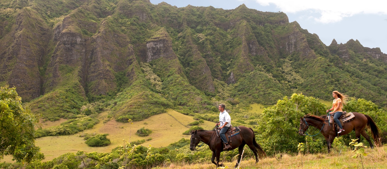 A man and a woman ride on horseback through a Hawaiian valley