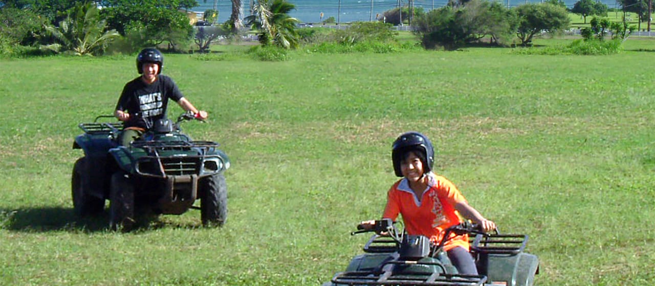 A teen boy and teen girl riding all terrain vehicles across a field