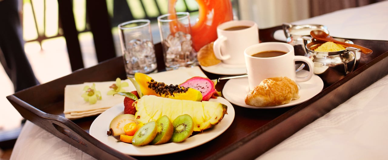A tray with a pitcher of juice, glasses, cups of coffee a croissant and fresh fruit