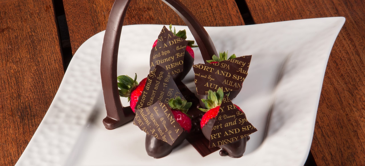 A plate of chocolate-dipped strawberries is presented with a chocolate version of the Aulani arch.