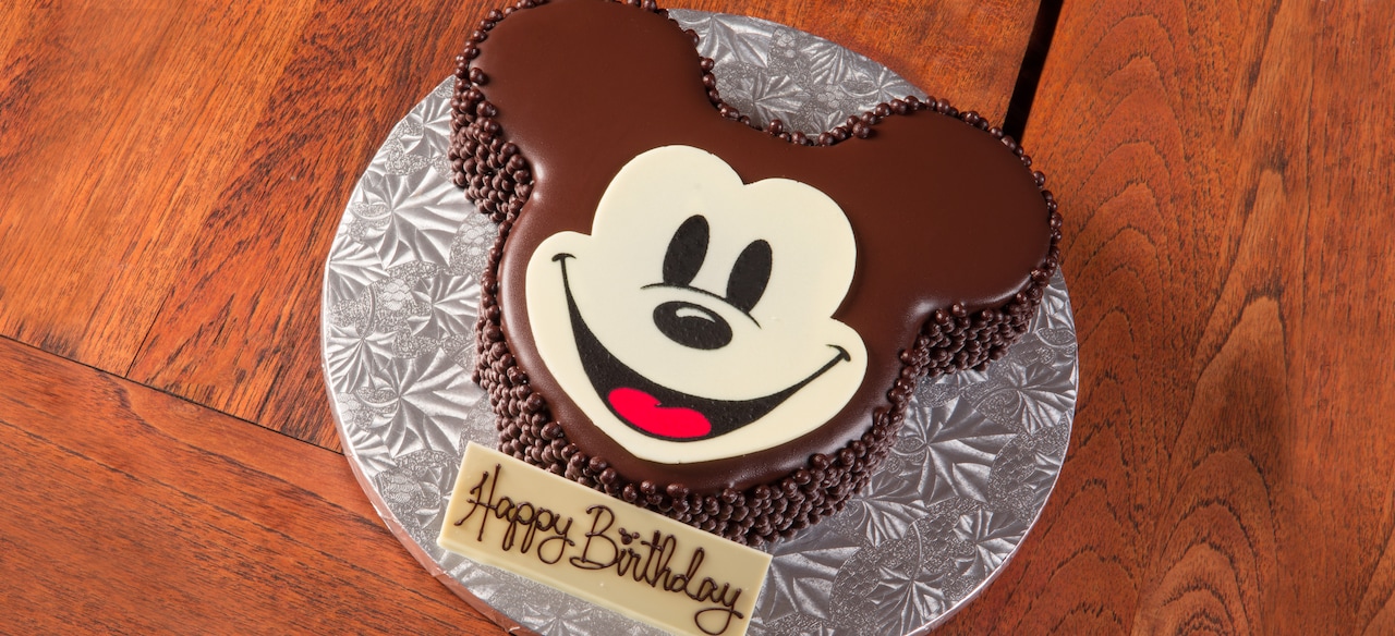 ミッキーマウスの形にデコレーションされた、「Happy Birthday (お誕生日おめでとう)」の文字入りのチョコレートケーキ