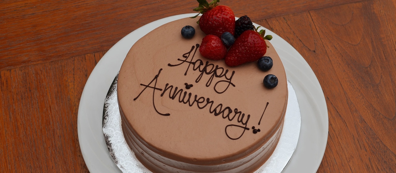 A cake with chocolate icing is decorated with strawberries, blueberries and "Happy Anniversary!" written in icing