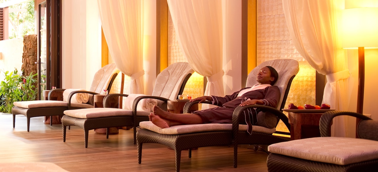 A woman in a spa robe relaxes in a lounge chair along a wall with white drapes and more lounge chairs
