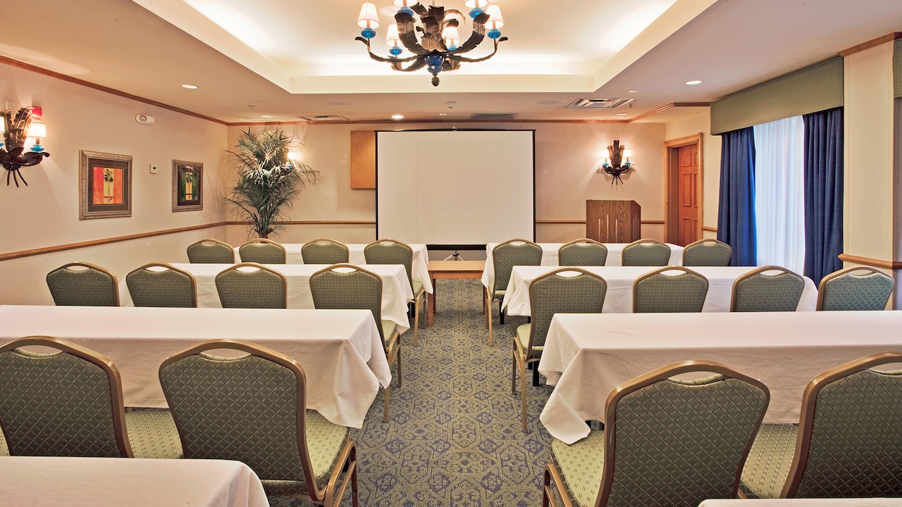 A meeting room with several tables with chairs facing a lectern next to a projection screen