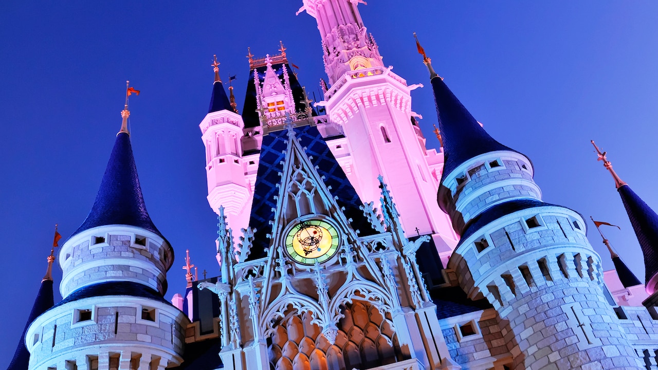 The towers and turrets of Cinderella castle, lit from all sides, stretch into the sky above Fantasyland