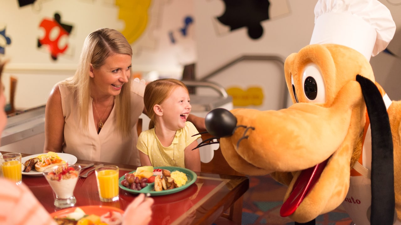 Niño y adulto sonríen, disfrutando a Pluto en una Comida con los Personajes