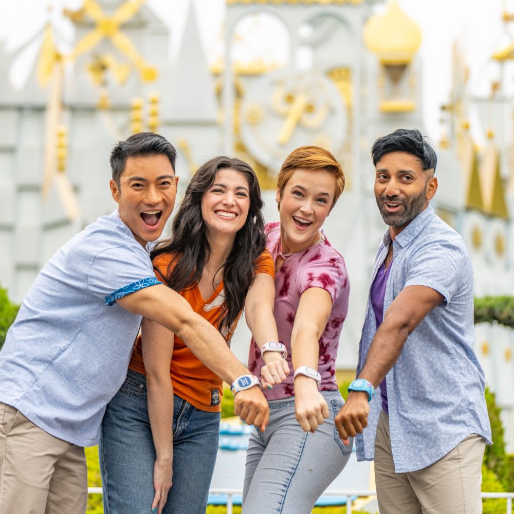4 adults holding out their wrists wearing Magic Bands