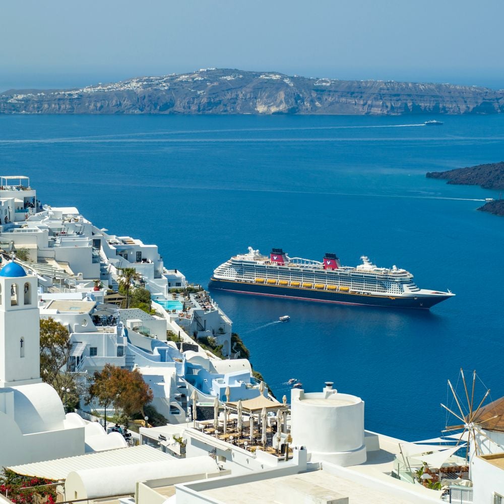 Buildings lining the beautiful coast of the island of Santorini, Greece, and a Disney Cruise Line ship in the water