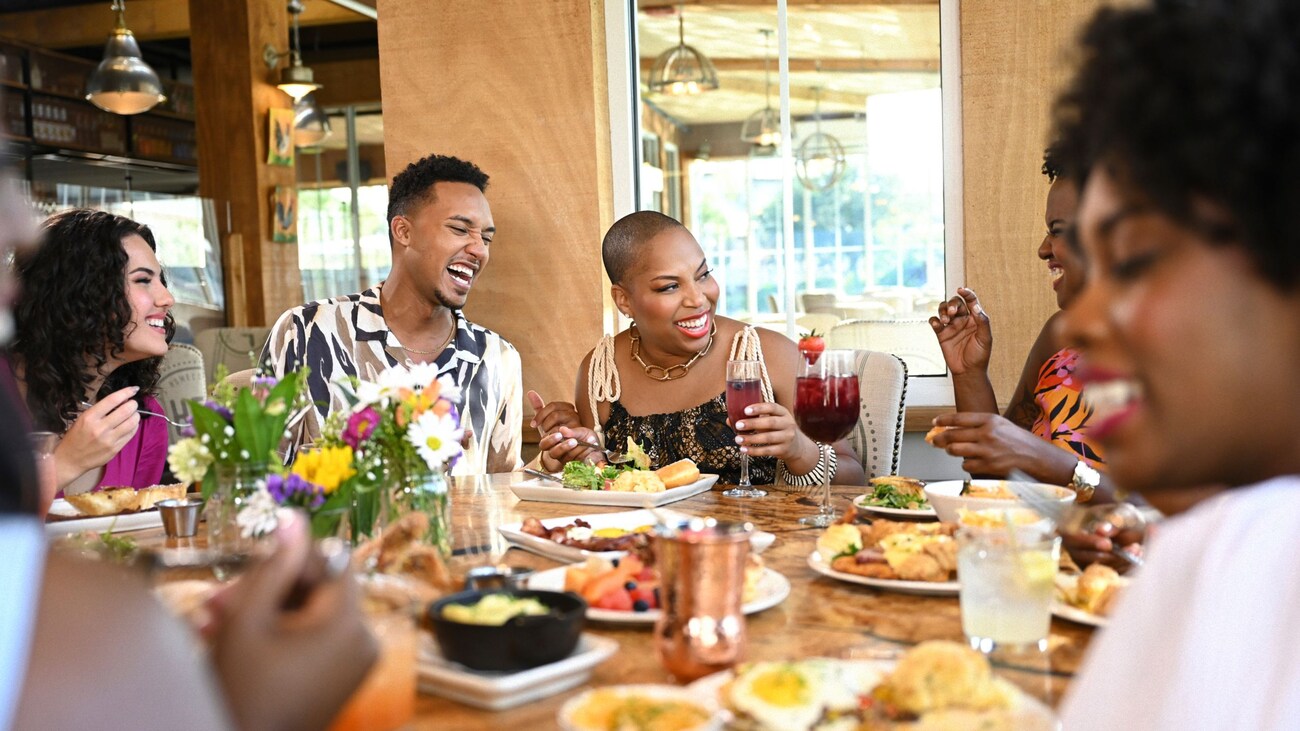 Un grupo de personas sonrientes cenando en el restaurante Chef Art Smith’s Homecomin’ con platos de comida y bebidas mezcladas