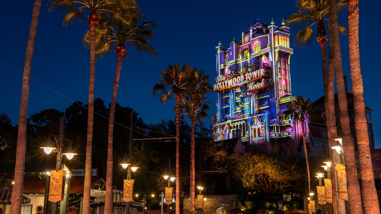 The Hollywood Tower hotel lit up at night and flanked by rows of palm trees