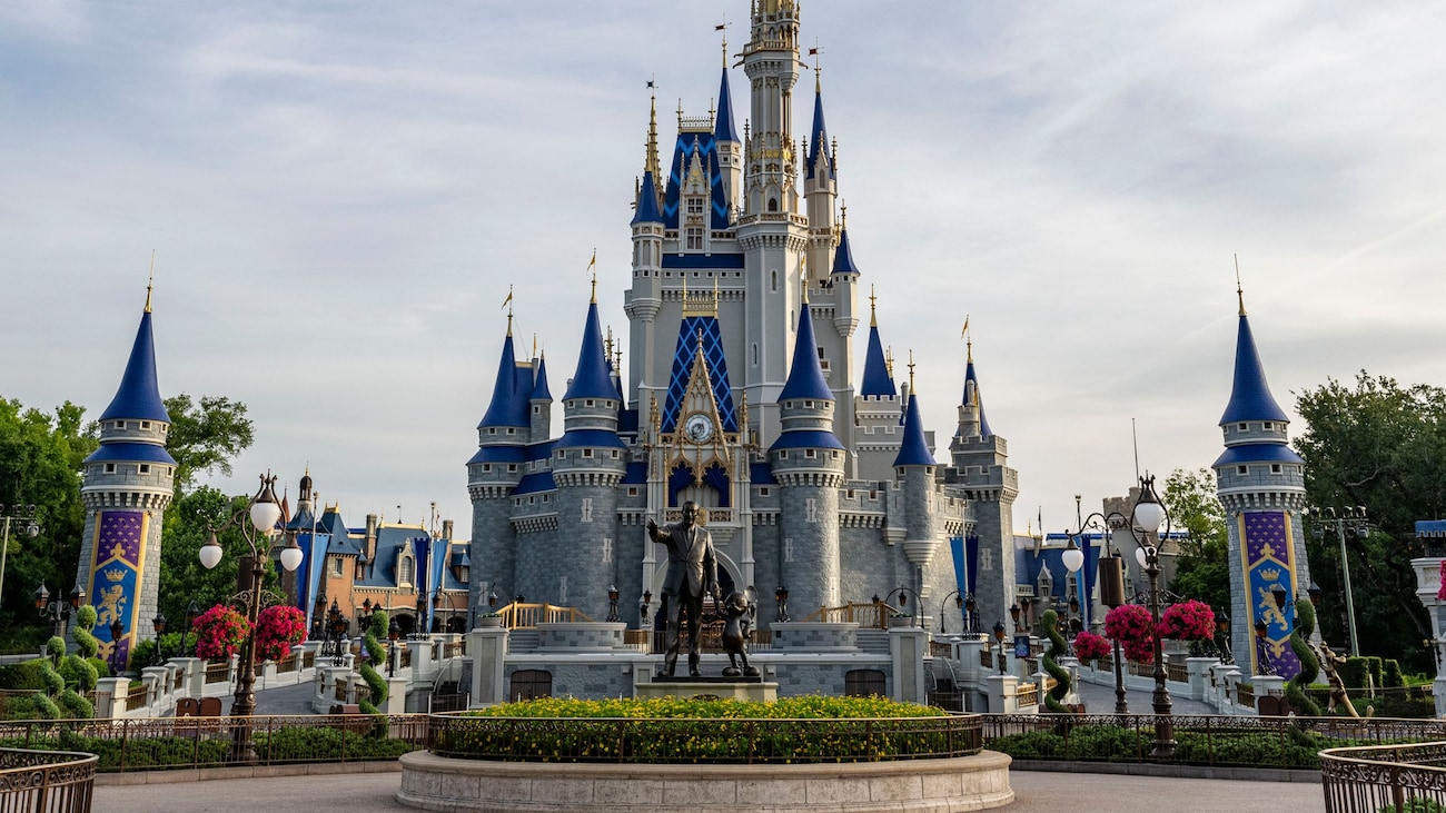 A statue of Walt Disney and Mickey Mouse in front of Cinderella Castle