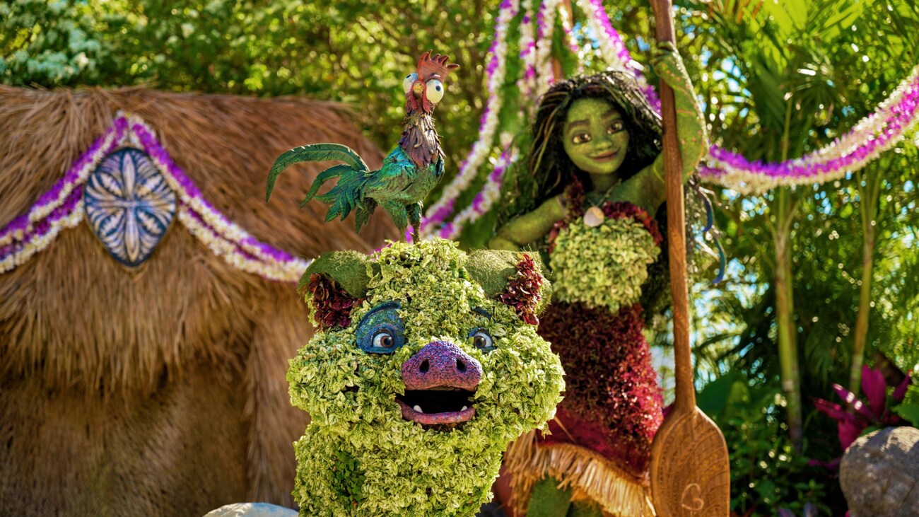 Detailed topiary representations of Moana, Hei Hei the rooster and Pua the pig standing in front of Moana’s hut