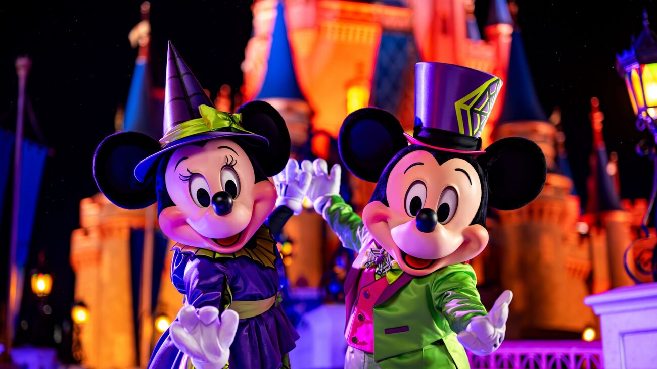 Minnie Mouse y Mickey Mouse vestidos con atuendos de Halloween posando frente al Cinderella Castle.