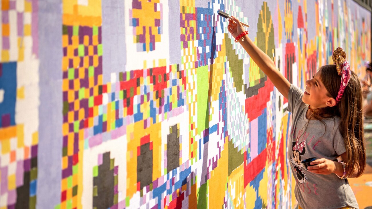 A girl in Disney themed apparel painting on a mural with geometric shapes