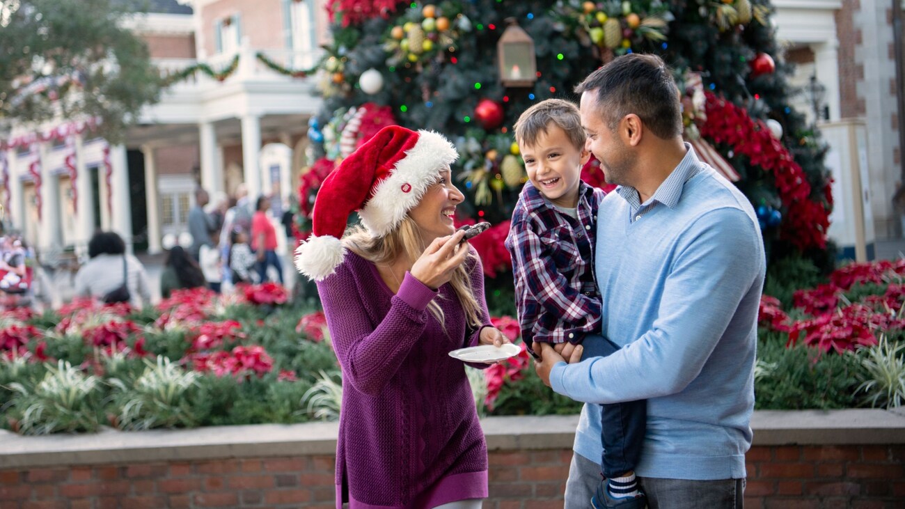 Two parents and their son eating Christmas cookies in front of a Christmas tree at The American Adventure at Epcot
