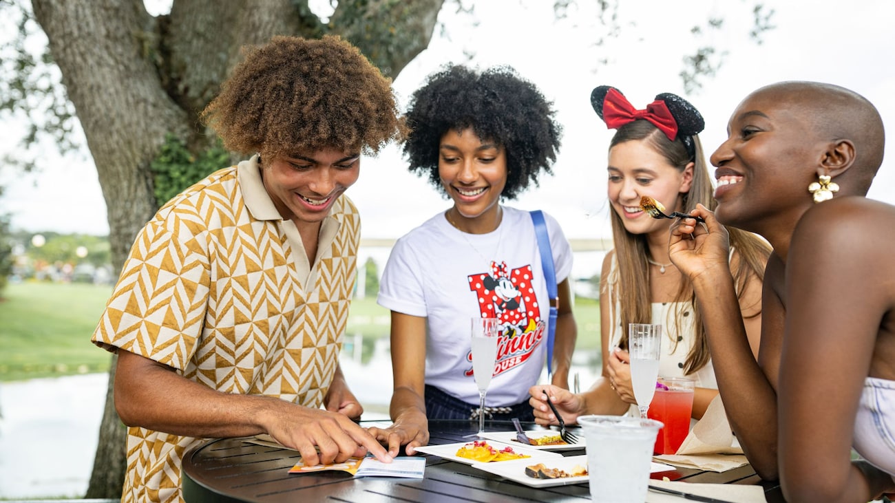 Guests enjoy food and drinks outdoors while looking at their Festival Passport at the EPCOT International Food & Wine Festival