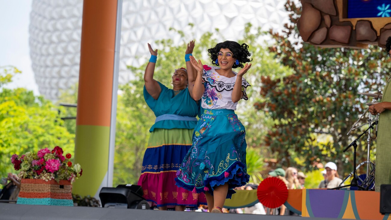 Mirabel Madrigal claps and sings with a performer onstage at the Celebración Encanto stage show