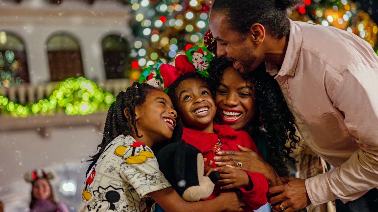 Una familia de 4 integrantes se abraza con expresiones de alegría en Main Street, USA decorada para las fiestas