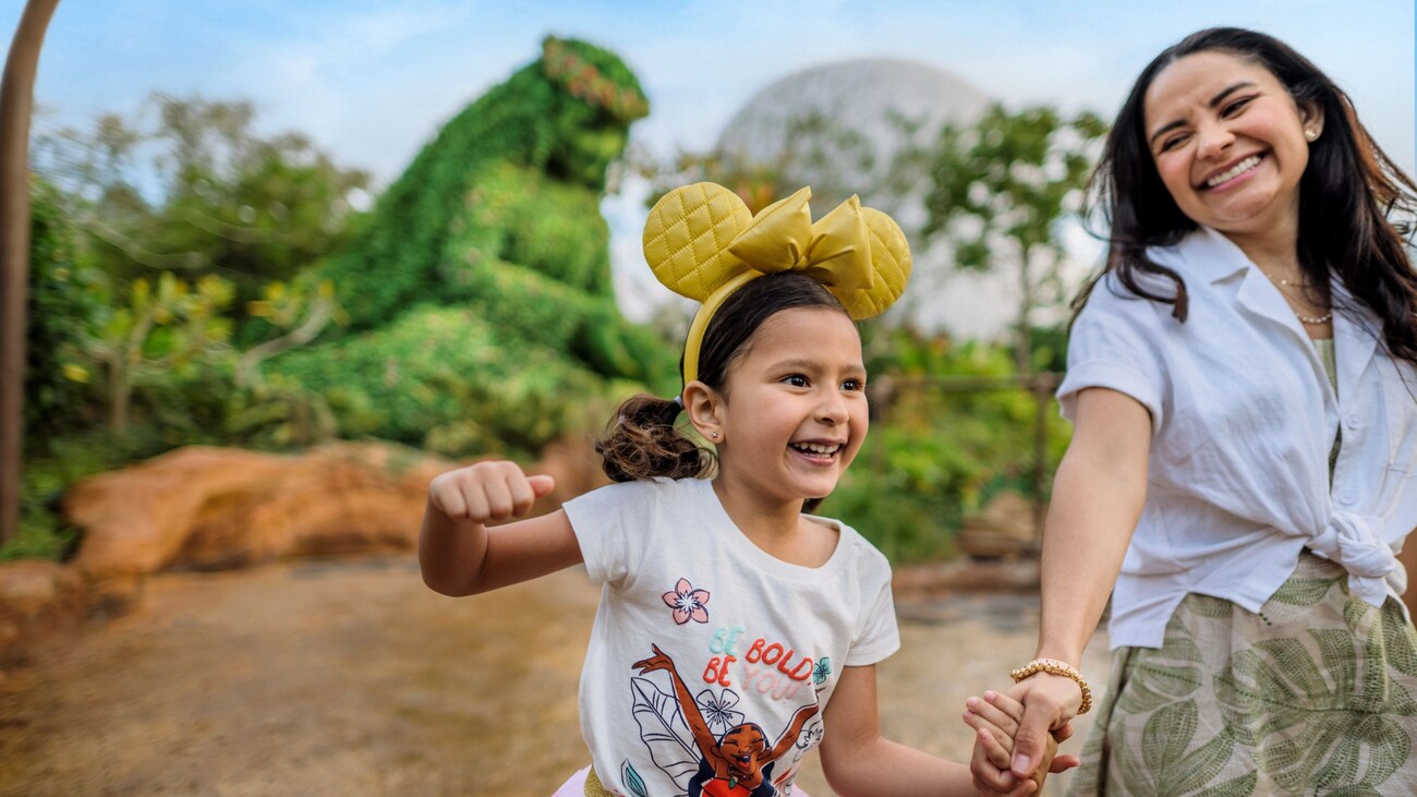 A girl wearing a Minnie Mouse ear headband holding hands with her mother in front of a topiary of Te Fiti