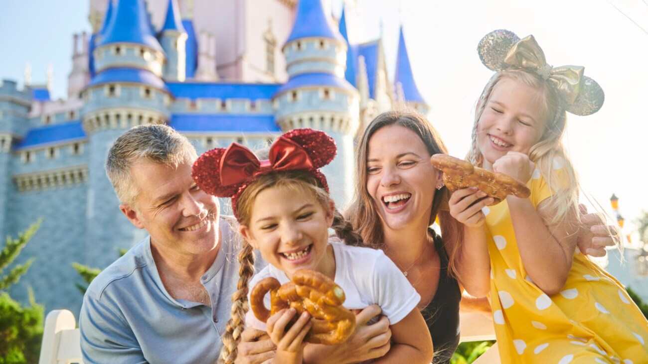 A family laughing together as they enjoy Mickey shaped pretzels in front of Cinderella Castle at Magic Kingdom park