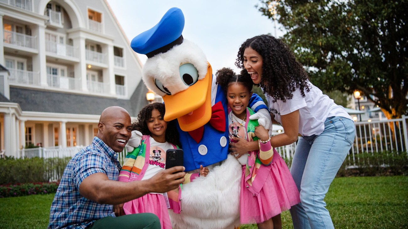 A family of 4 taking a selfie with Donald Duck in front of Disney’s Yacht Club Resort 