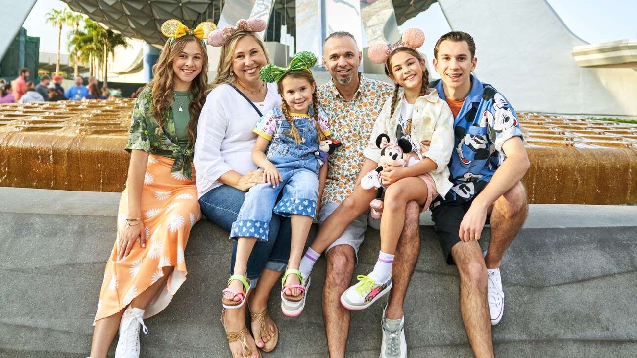 A family smiling and sitting on the edge of the fountain in front of Spaceship Earth at Epcot