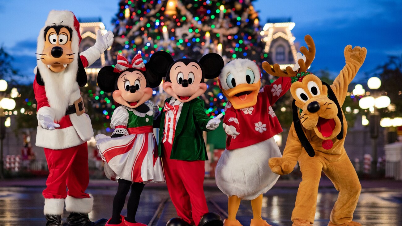 Goofy, Minnie Mouse, Mickey Mouse, Donald Duck y Pluto con atuendos navideños y posando frente al árbol de Navidad en Main Street USA