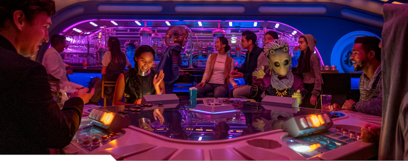 Various Guests play games and interact with Characters from foreign planets in a lounge aboard the Halcyon starcruiser