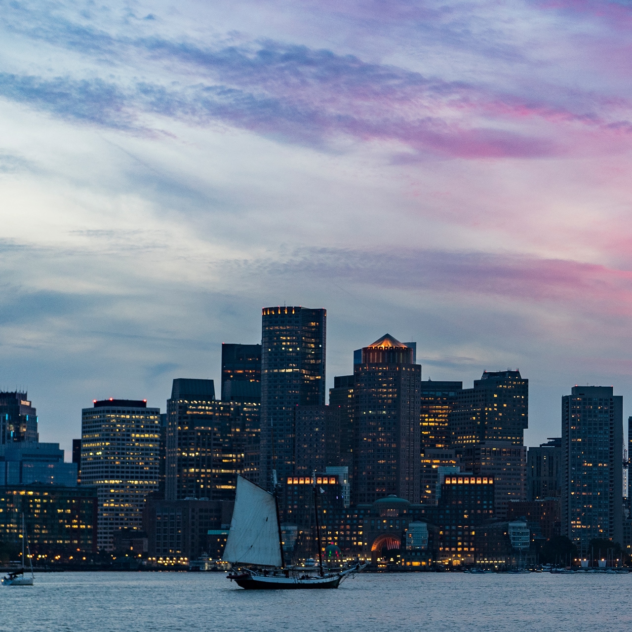 A boat on the Charles River in front of the Boston skyline at dusk