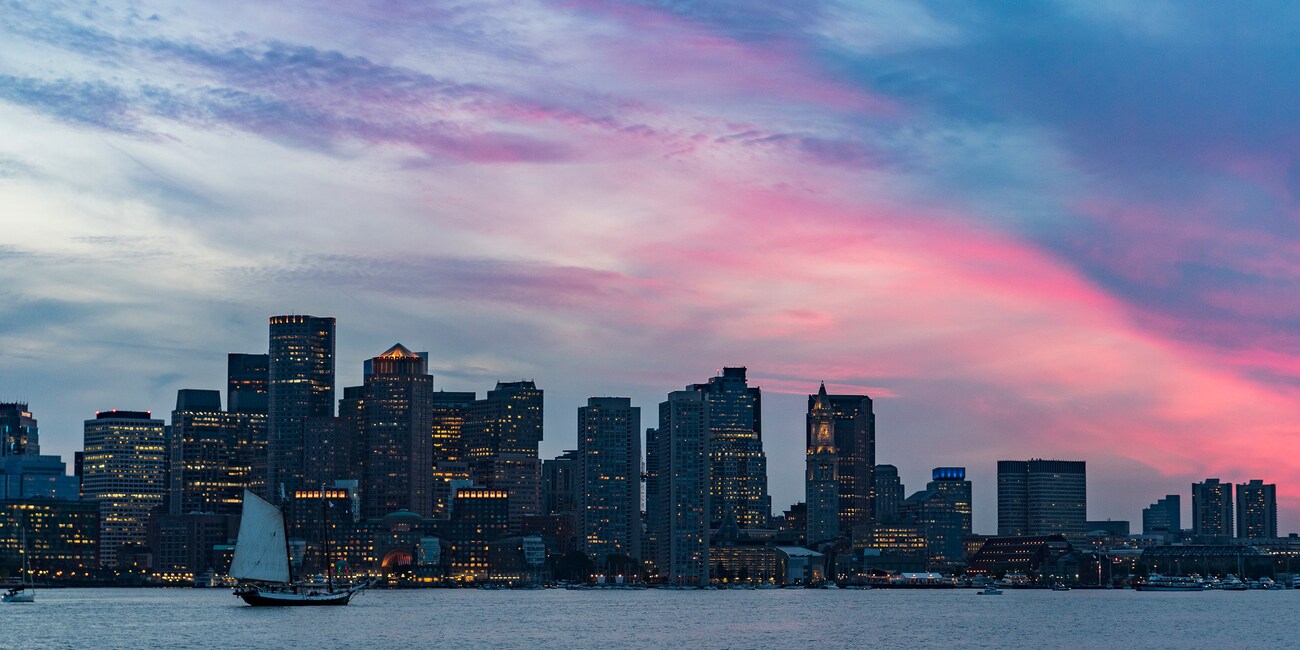 A boat on the Charles River in front of the Boston skyline at dusk