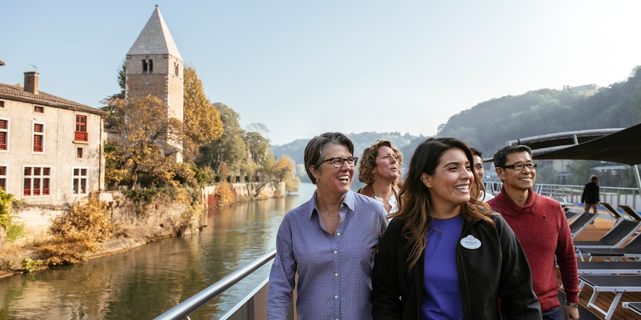 An Adventure Guide and 3 Adventurers pass a stone building and tower as they sail down the Rhône River
