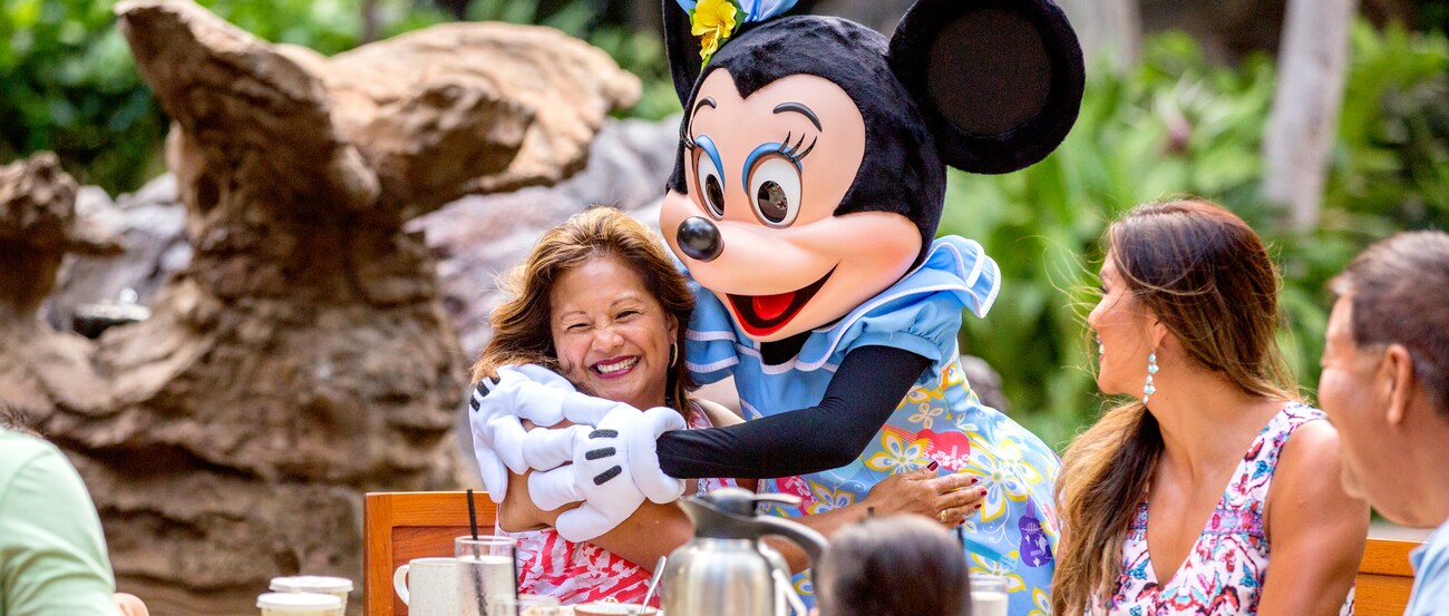 キャラクター・ダイニングで、耳に花を飾り笑顔の女性の膝に座るミニーマウス