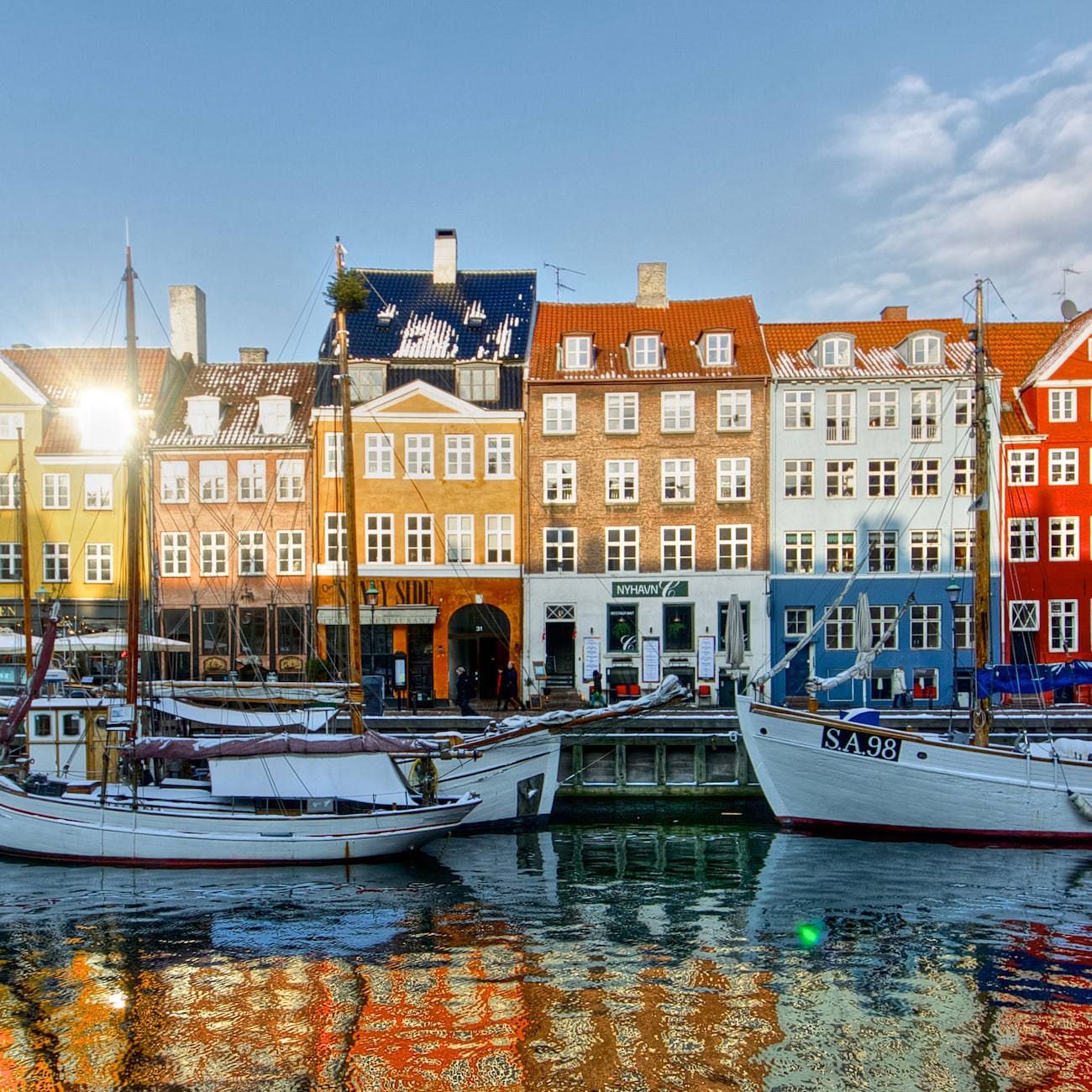 Sailboats are docked at the Copenhagen harbor near European row houses