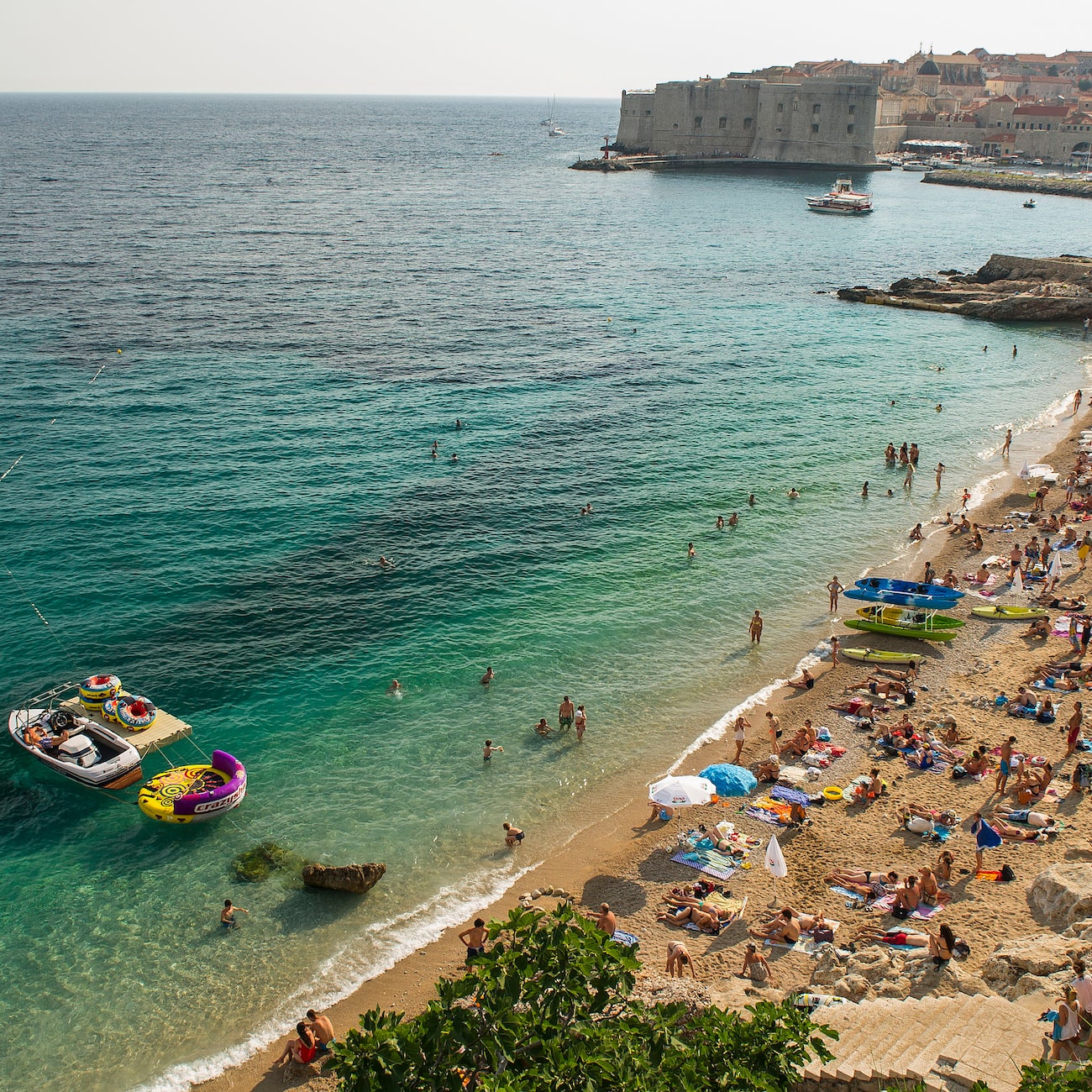 Beach-goers at Banje Beach in Dubrovnik, Croatia, with buildings in the background
