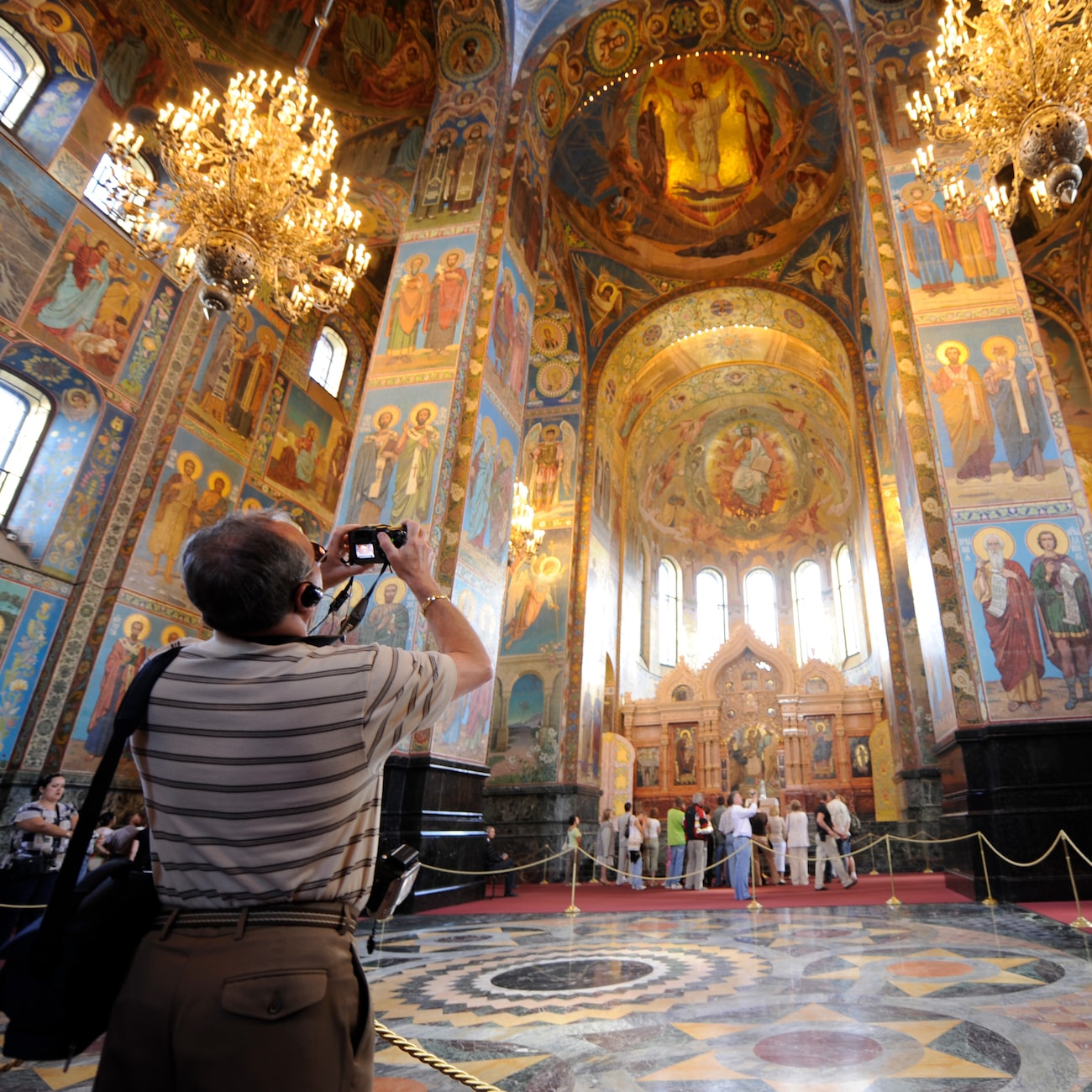 A man takes a photo of the murals and ornate interior décor of the Church of the Savior on Spilled Blood in St. Petersburg, Russia