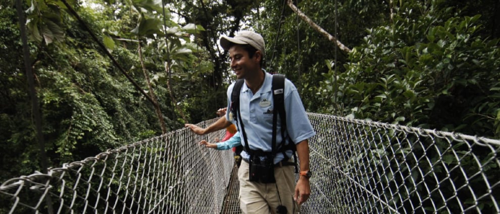 An Adventure Guide leads a family over a pedestrian bridge surrounded by trees 