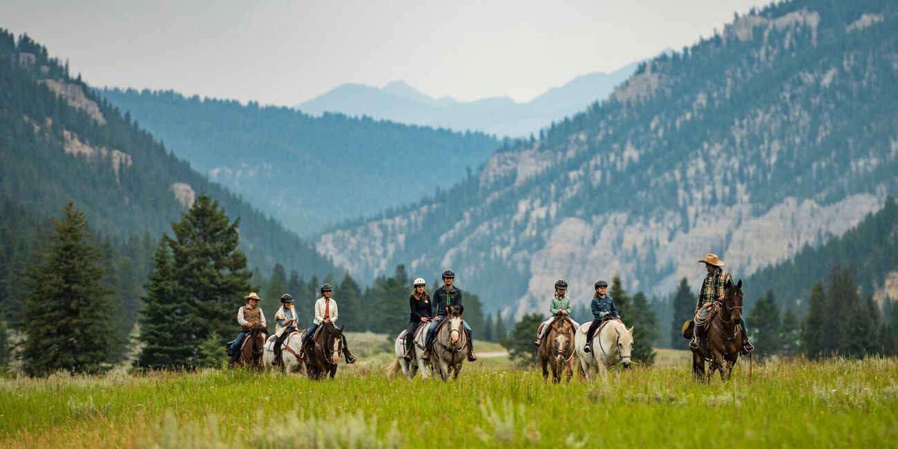 A group of people ride horses on the grassy plain of a mountain valley