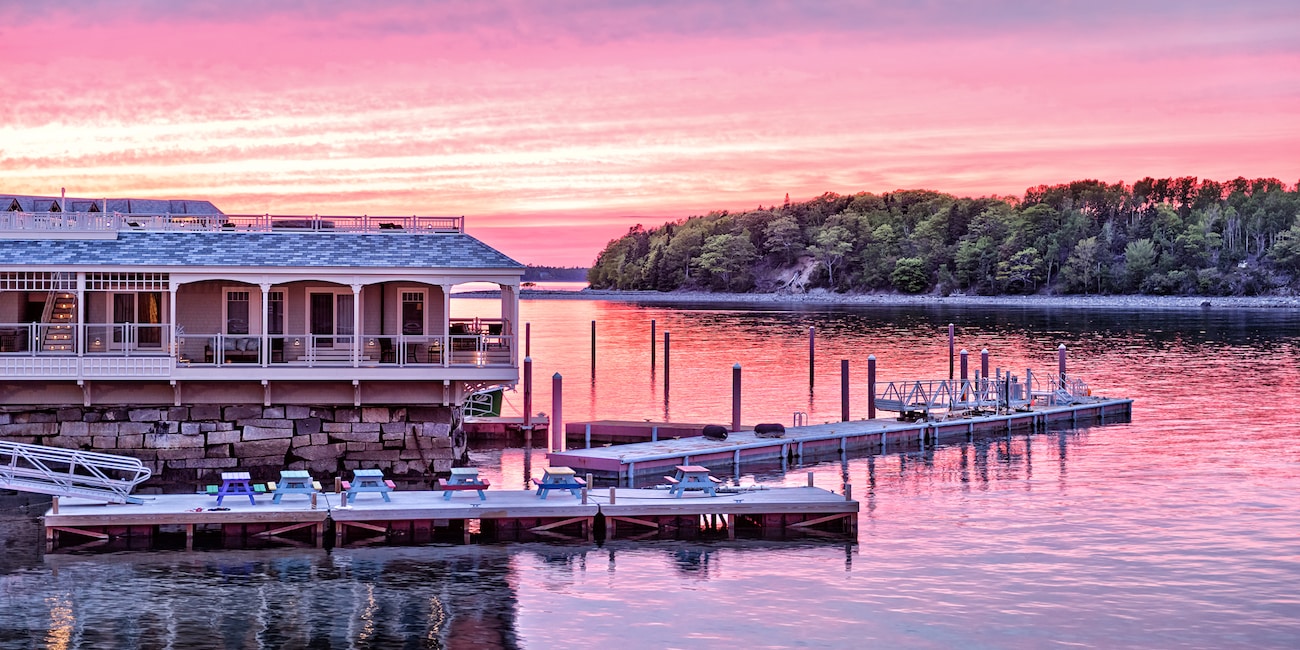 A house on the water in Bar Harbor, Main sits across the lake from a forest-lined river bank at sunset