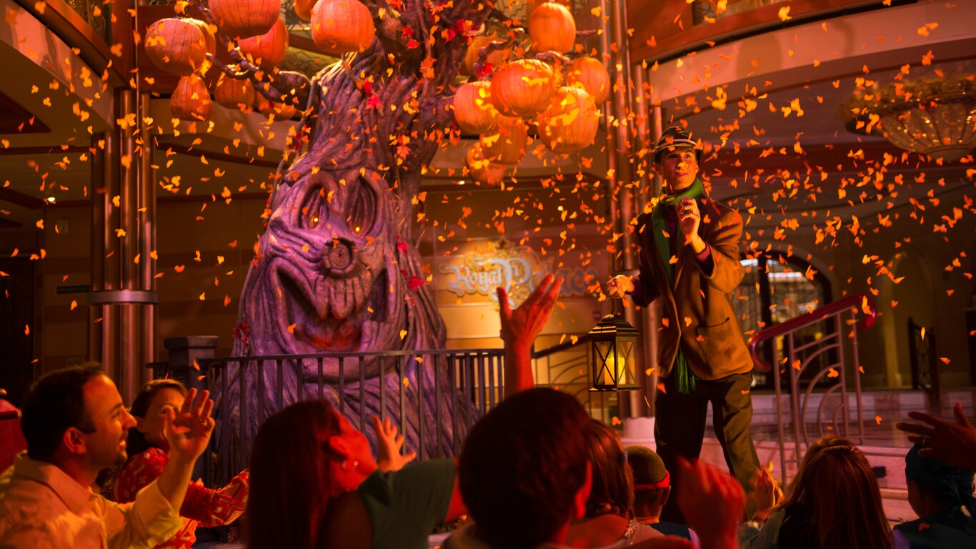 Families watch a Halloween themed show with a spooky tree, jack o lanterns, orange light and confetti