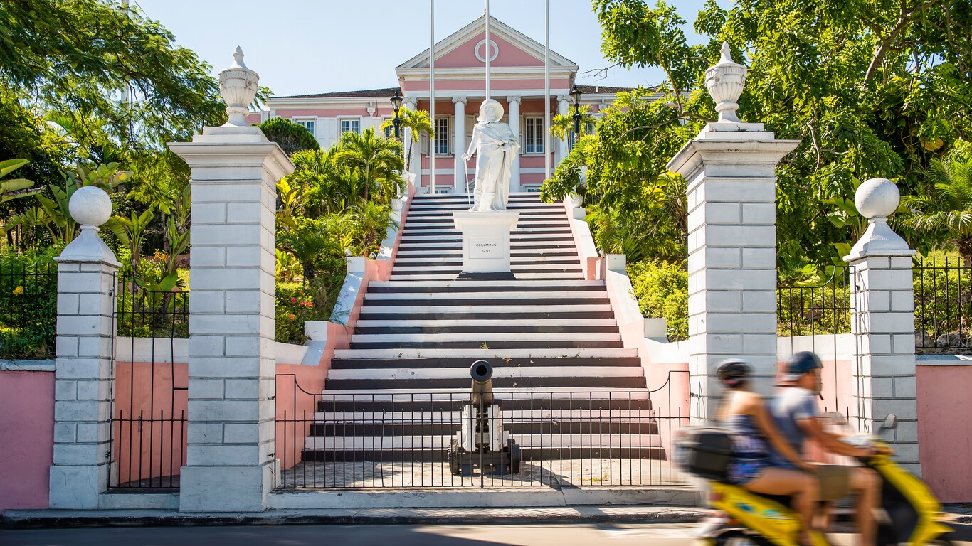 Behind a low fence and a cannon, stairs lead up past a statue to a large house with columns