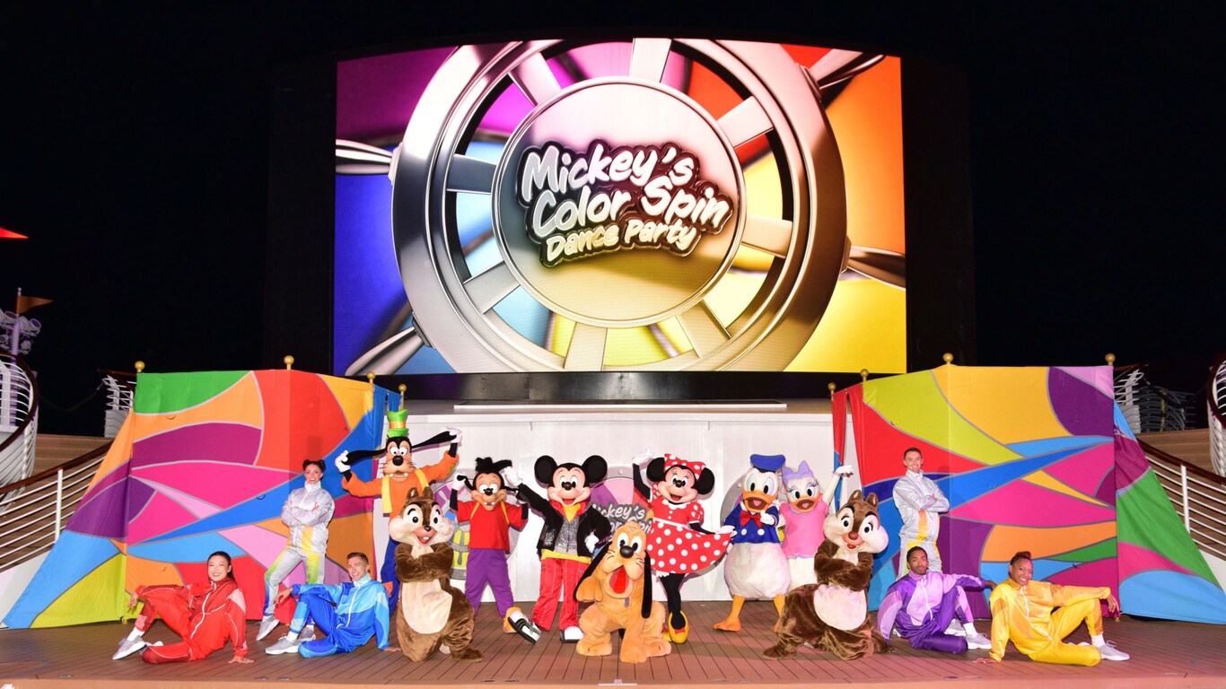 A scene from Mickey’s Color Spin Dance Party featuring Disney Characters and Cast Members posing for a picture on the Funnel Vision Deck Stage of a Disney Cruise Line ship