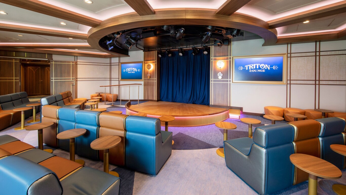 An auditorium at the Triton Lounge with a stage, upholstered seating and small tables